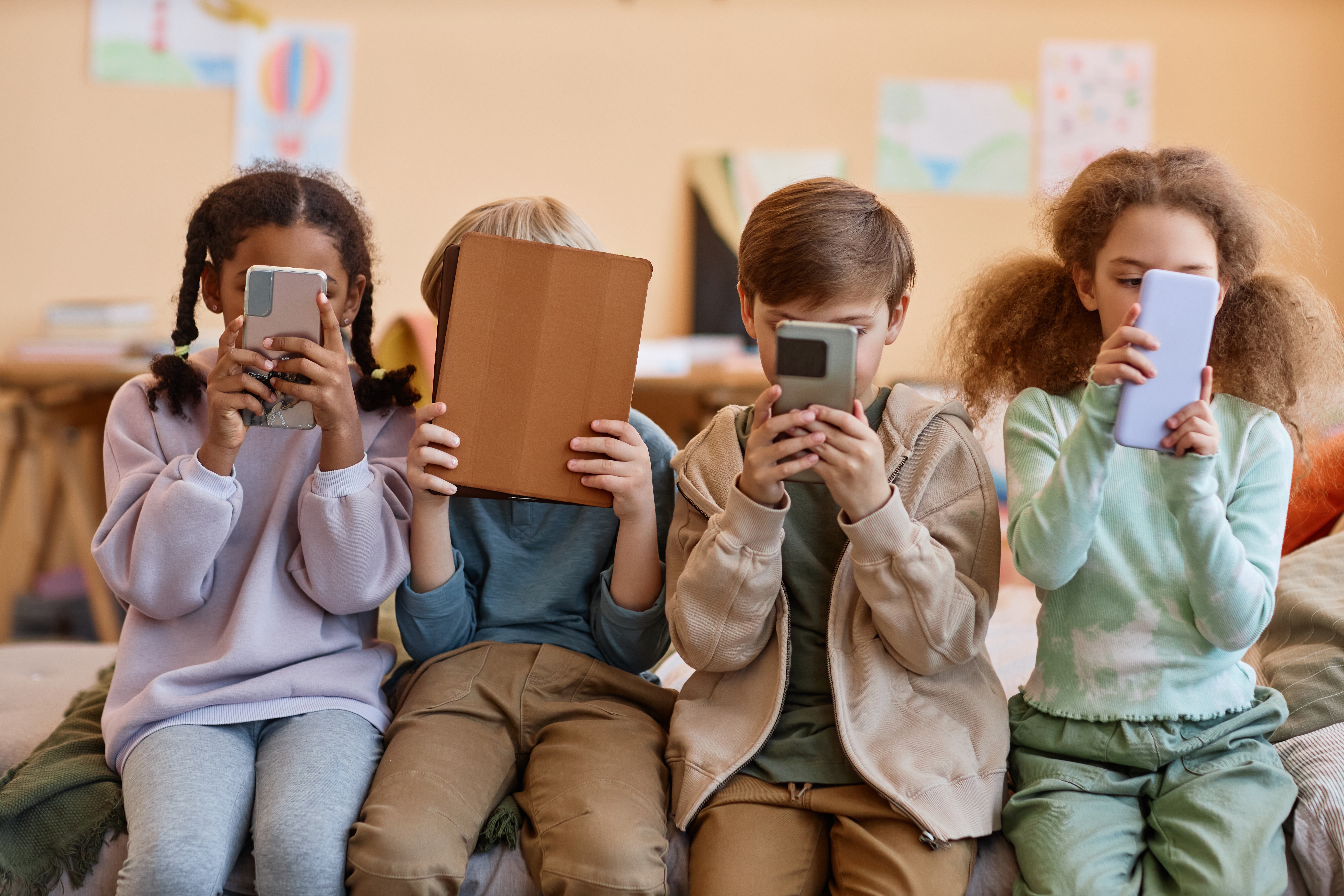 Das Bild zeigt eine Gruppe von Kindern, die jeweils ein Mobilgerät in Händen halten und damit ihre Gesichter verdecken. ©Seventyfour - stock.adobe.com